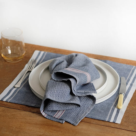 Dining table setting with blue napkin, white plates, and striped placemat.