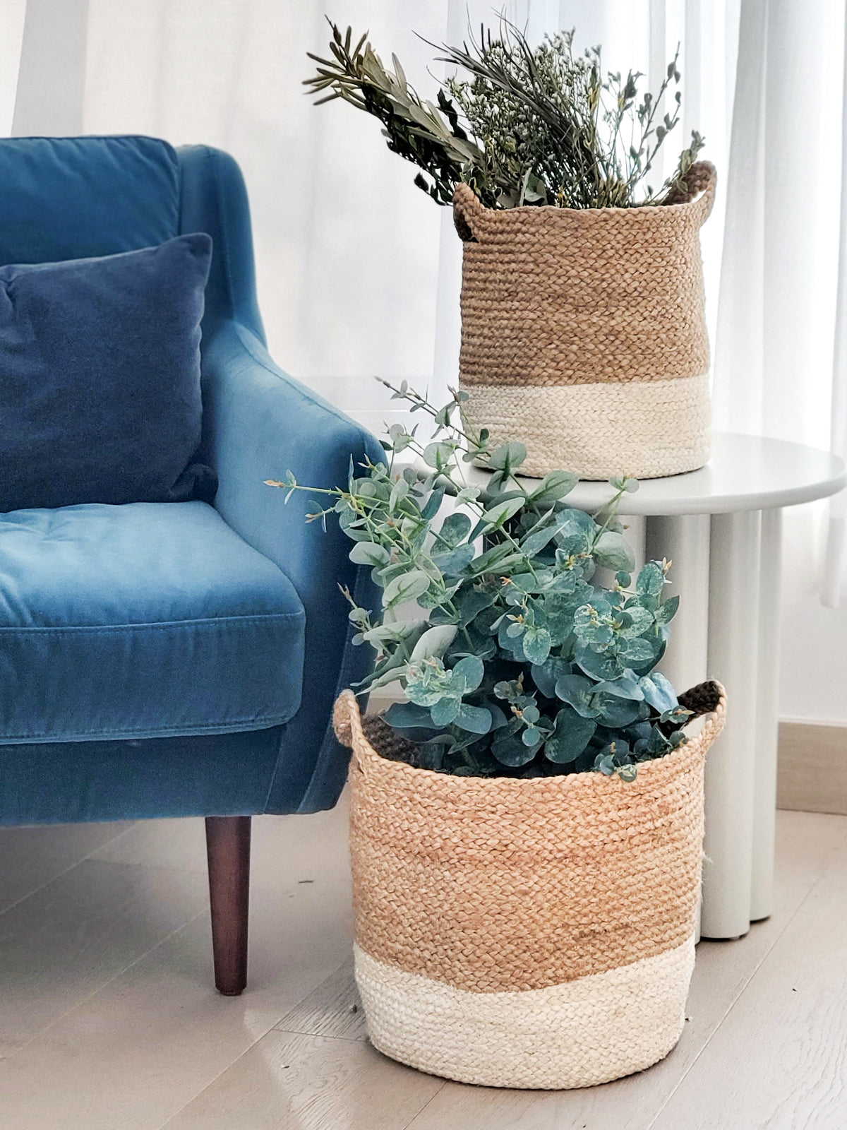 Woven planters with plants on a light-colored floor next to a blue armchair.