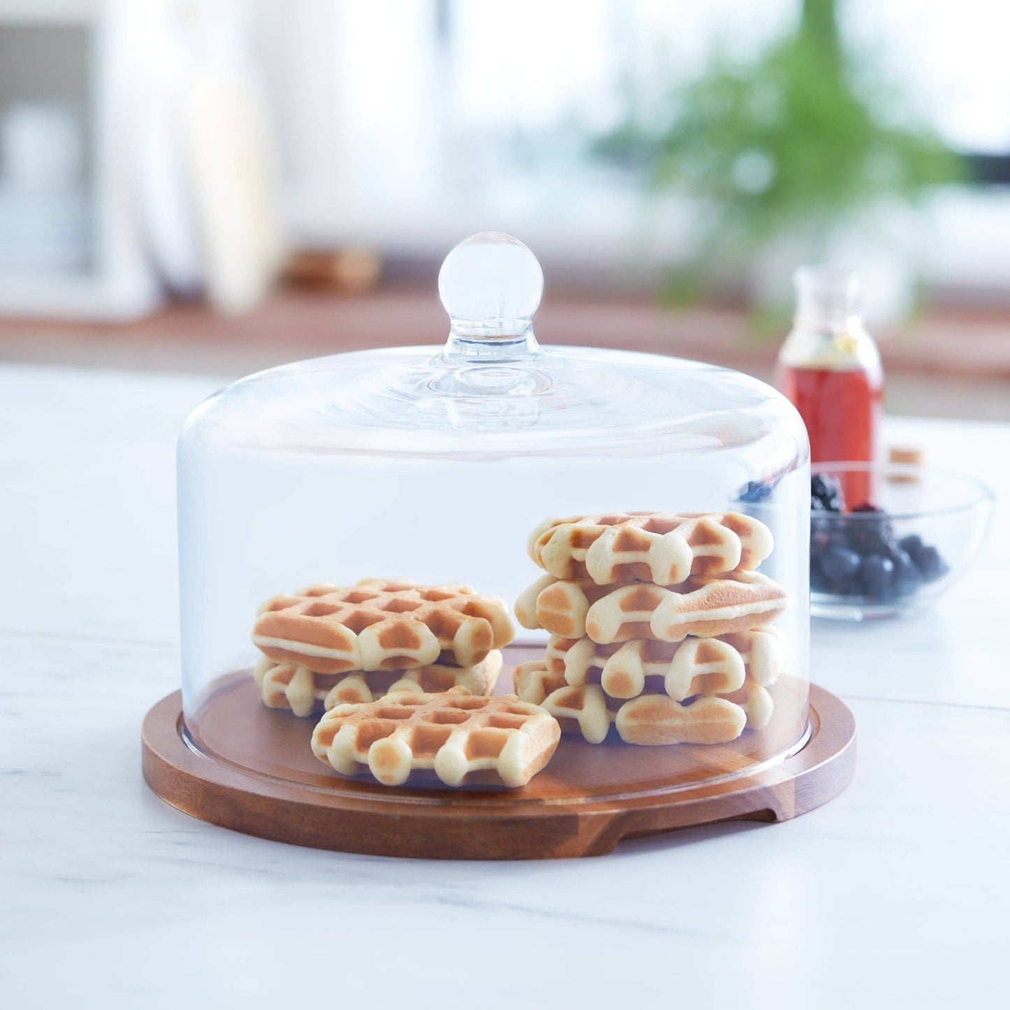 Glass cake stand with waffles on a wooden base in a kitchen setting