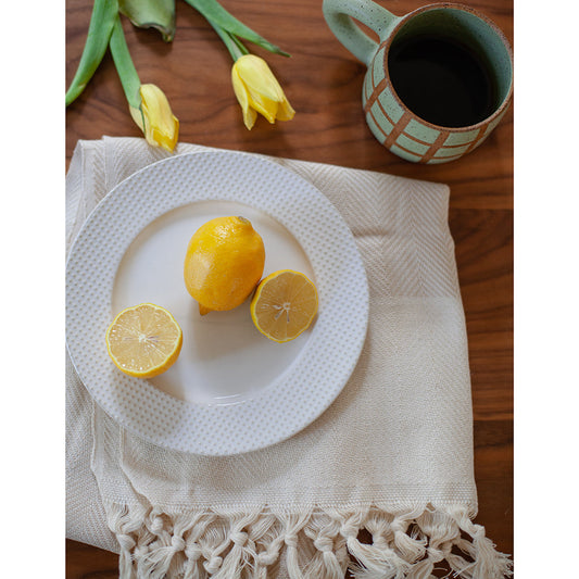 Three lemons on a white plate with a mug of coffee and yellow tulips in the background.