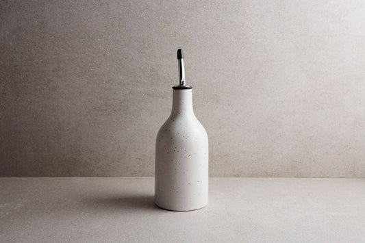 White ceramic bottle with a black cap on a light gray surface and background